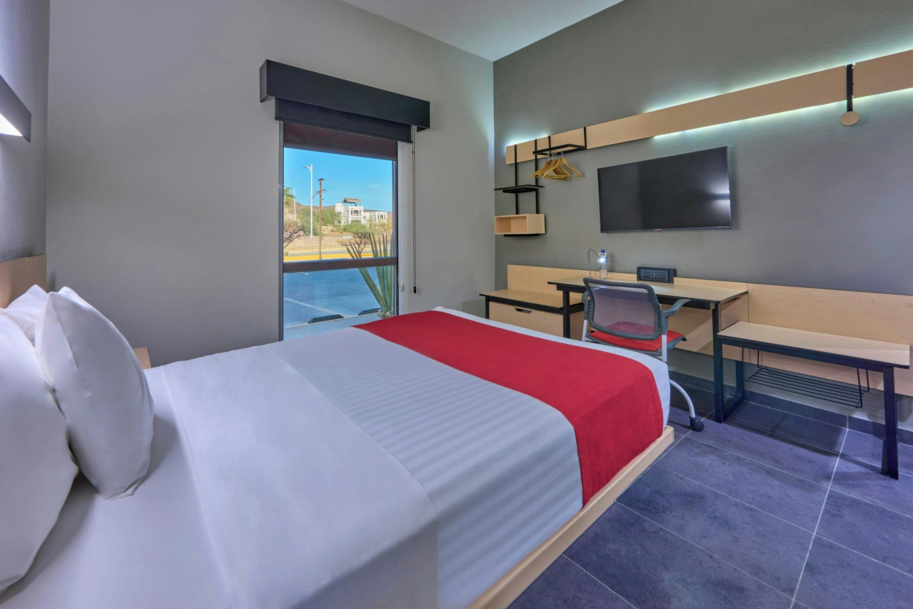 A hotel room with a bed, desk, chair, and a TV mounted on the wall.