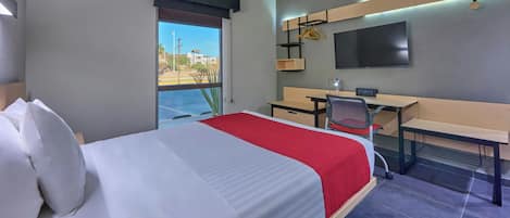 A hotel room with a bed, desk, chair, and a TV mounted on the wall.
