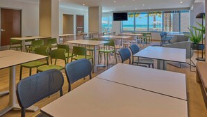 Un'area pranzo moderna con diversi tavoli e sedie, una TV a schermo piatto montata a parete e vista sulla spiaggia attraverso ampie finestre.
