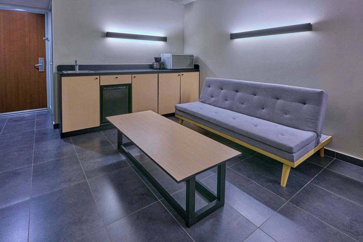 Una kitchenette moderna con un sofá gris y una mesa de madera.