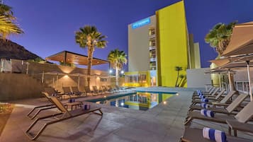 Zona de piscina de hotel con tumbonas y un edificio con la leyenda 'City Express'.