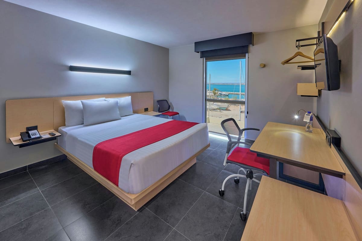 Habitación de hotel con cama, mesita de noche, silla, escritorio y vistas al mar.