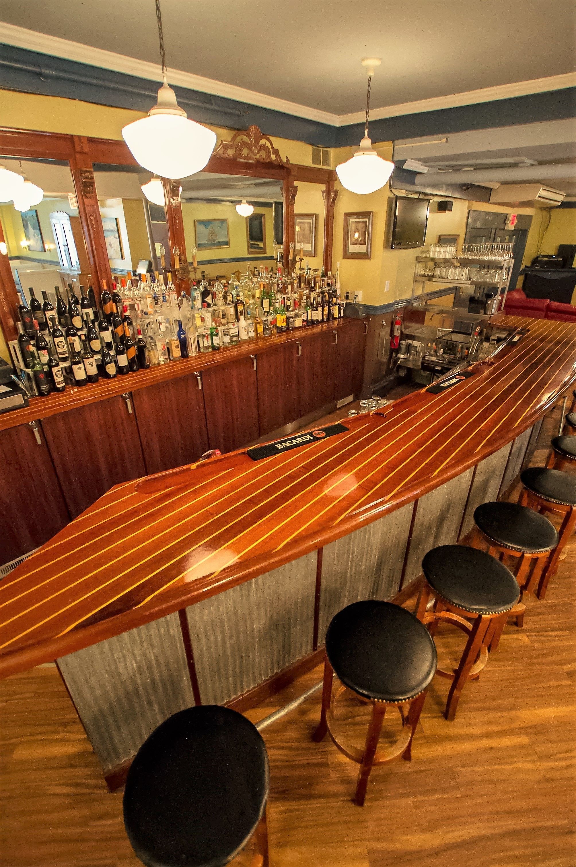 A bar area with a long counter, multiple stools, and a variety of bottles and glasses.