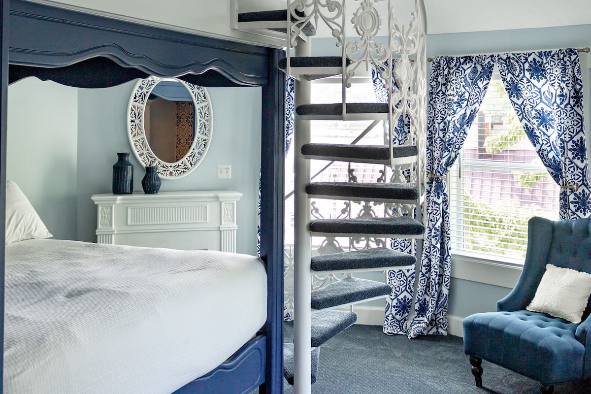 Een slaapkamer met een stapelbed, een decoratieve spiegel, een dressoir, een blauwe fauteuil en een wenteltrap.
