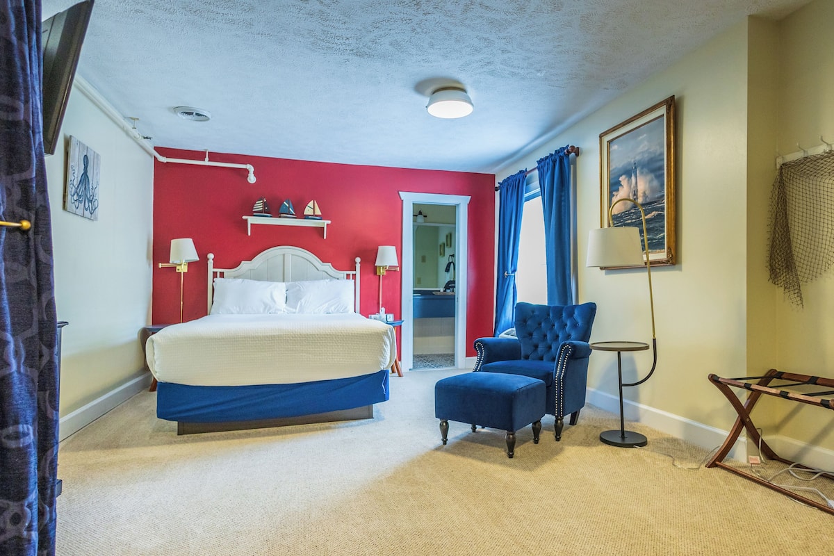 Een slaapkamer met een bed, een blauwe fauteuil, een tafeltje en een schilderij aan de muur.