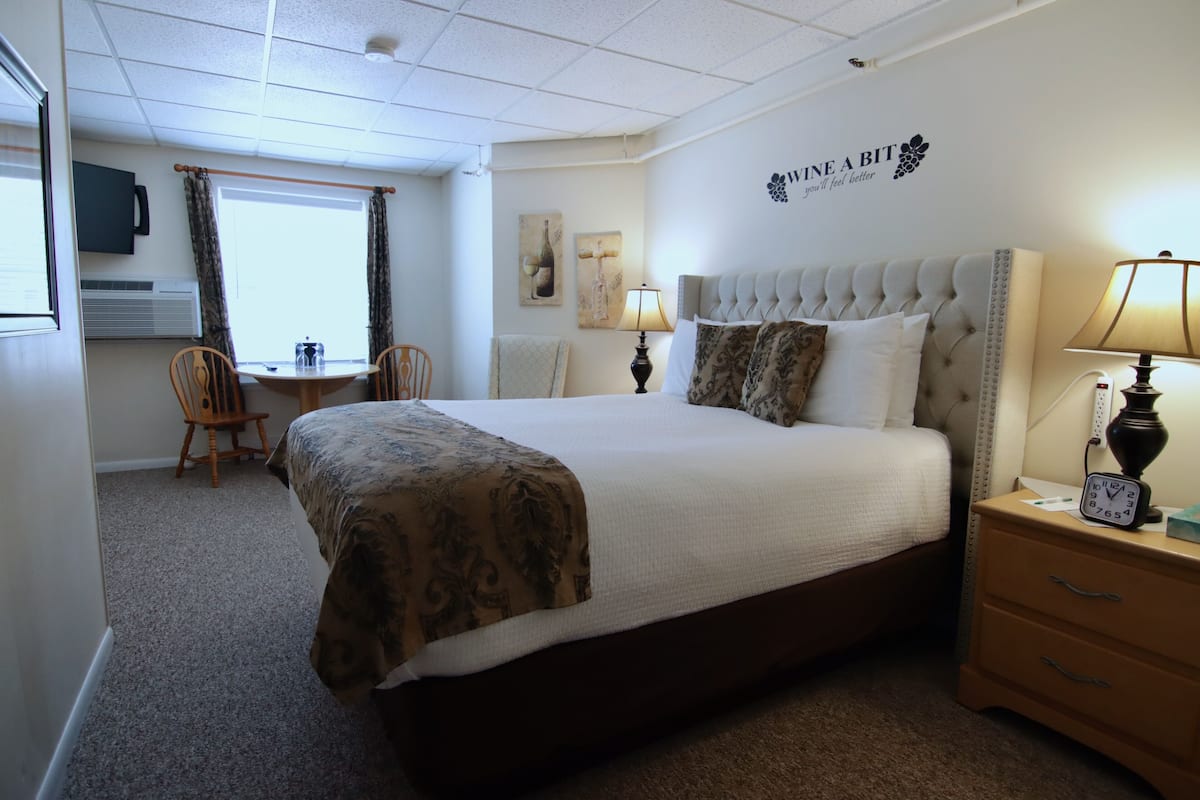 Een hotelkamer met een groot bed, een nachtkastje met een lamp, een bureau met een stoel en een raam met gordijnen.