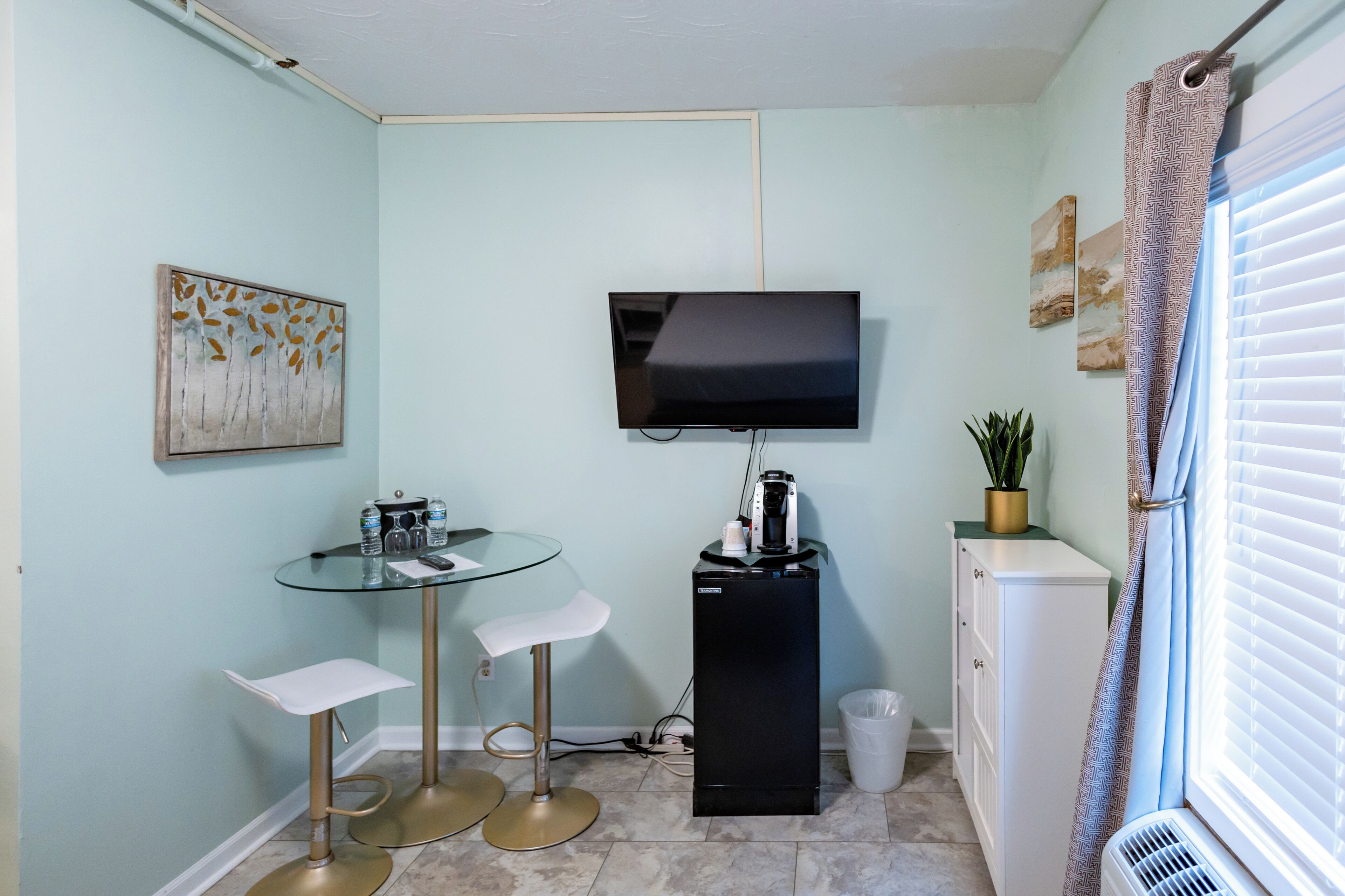 A compact living space with a TV, a small bar area with stools, a coffee machine, and a radiator.