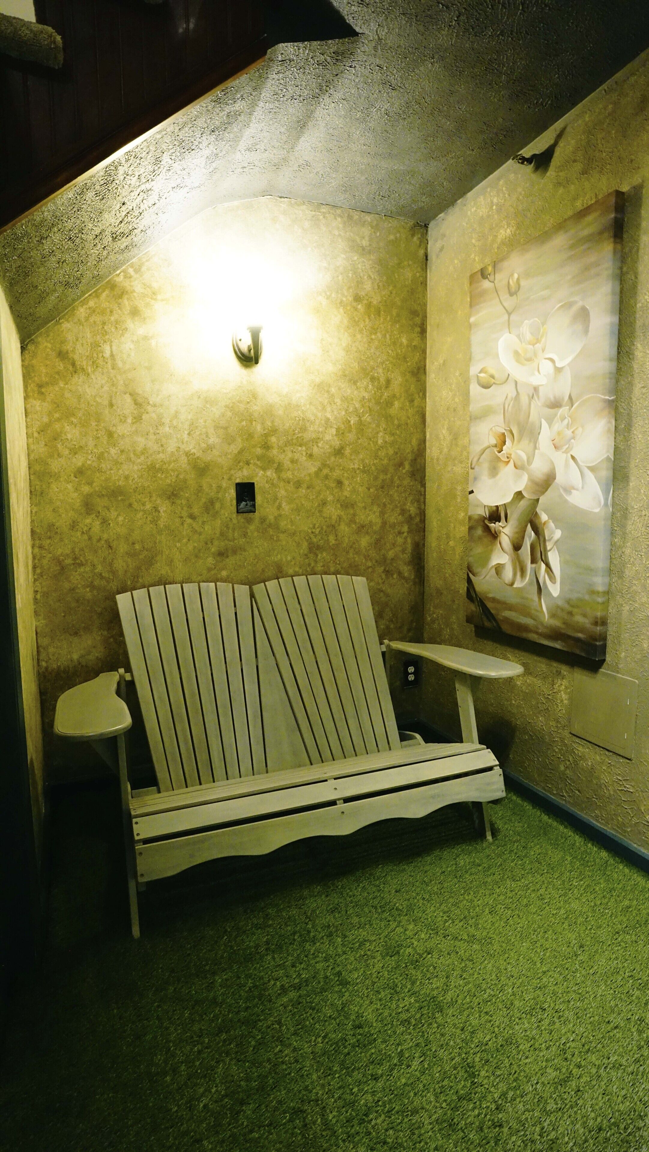 A small, cozy room with a single wooden bench, a small table, and a wall-mounted light fixture.