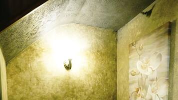 A small, cozy room with a single wooden bench, a small table, and a wall-mounted light fixture.