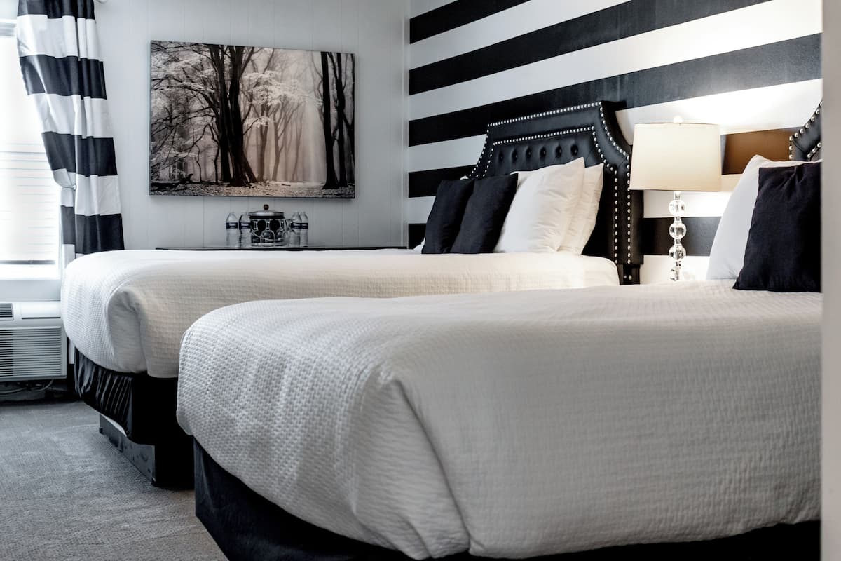 Een hotelkamer met twee bedden, een groot schilderij aan de muur en een nachtkastje met een lamp.