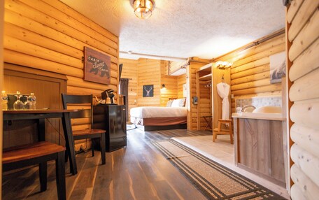 A cabin interior with a wooden floor, a bed, a table with chairs, a sink, and a shower area.