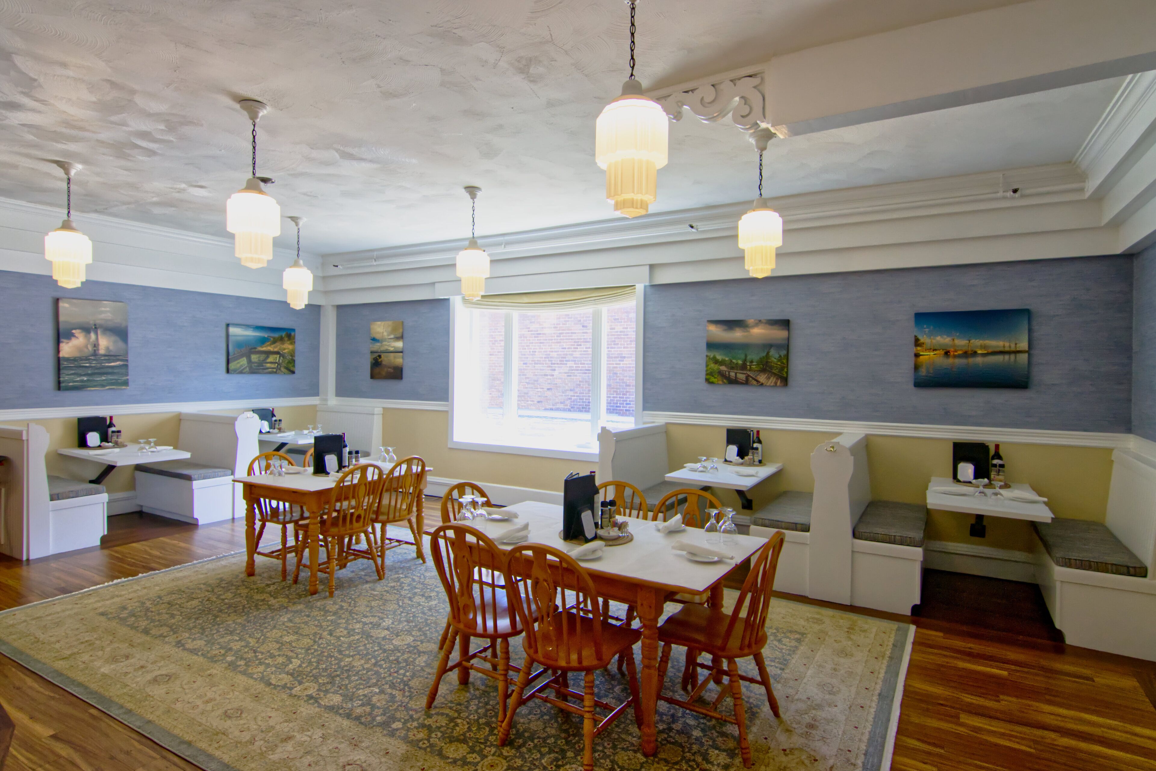 A dining area with wooden chairs and tables, a patterned rug, and pendant lighting.