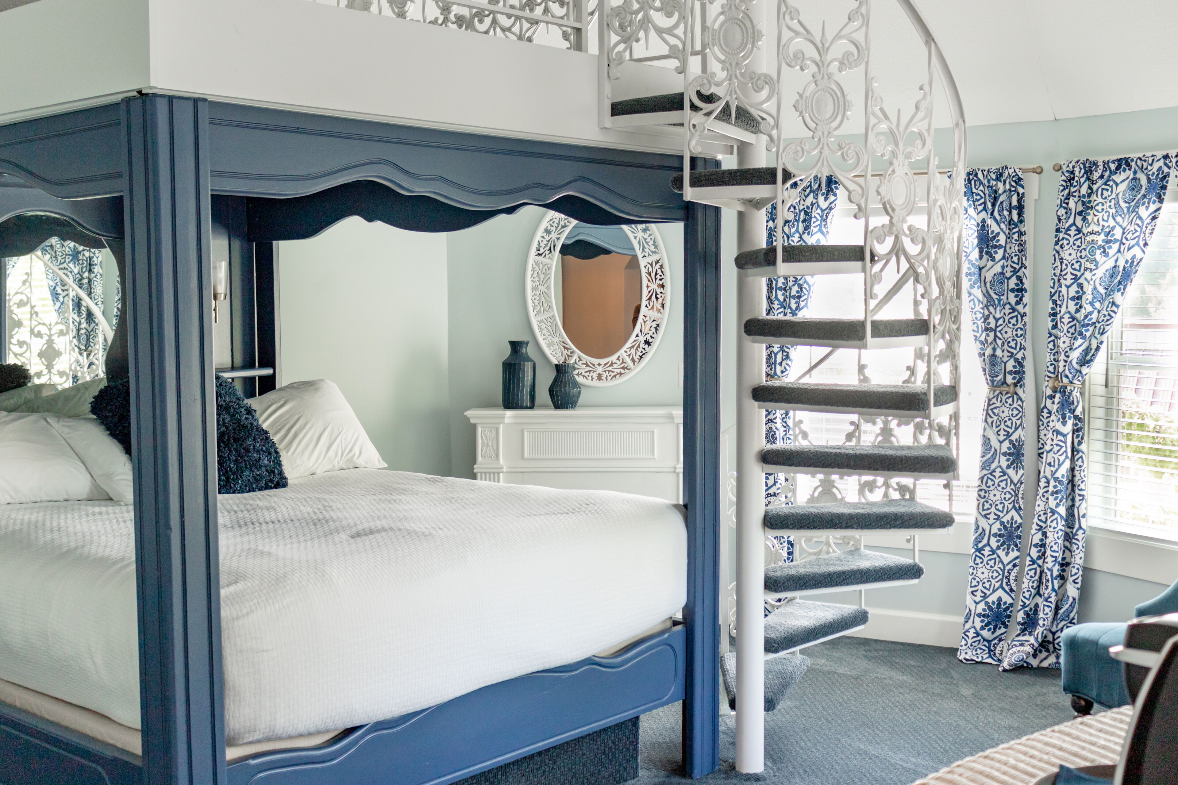 Une chambre à coucher avec un lit à baldaquin, une commode blanche, un miroir et un escalier en colimaçon.