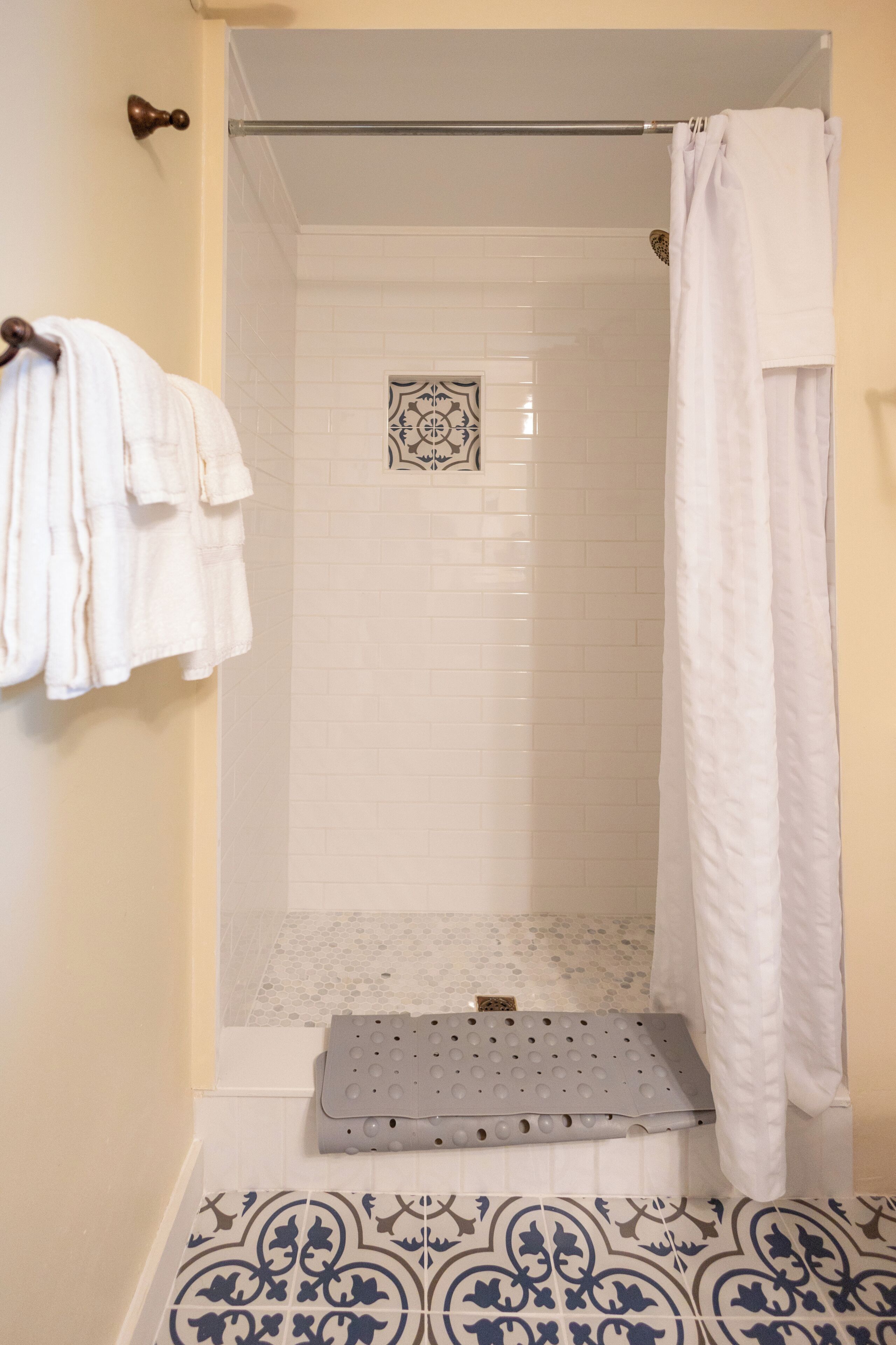 Een douchegedeelte met een betegelde muur, een douchegordijn en een trede naar de douche.