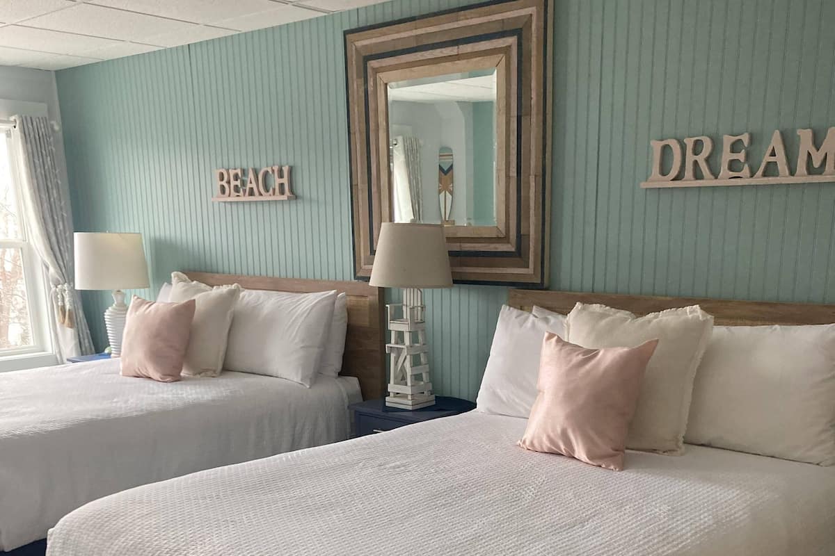 Een hotelkamer met twee bedden, een spiegel en een muur waarop 'BEACH' en 'DREAM' staan.