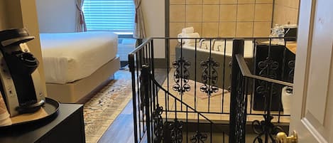A bedroom with a bed, a desk, a dresser, a bathroom with a bathtub, and a staircase.