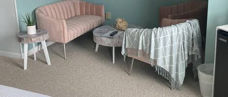 A room with teal walls, a pink sofa, a grey ottoman, a small side table with a plant, and a television mounted on the wall.