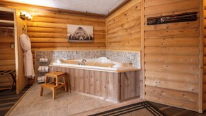A wooden cabin bathroom with a large bathtub, a wooden bench, and a towel rack.