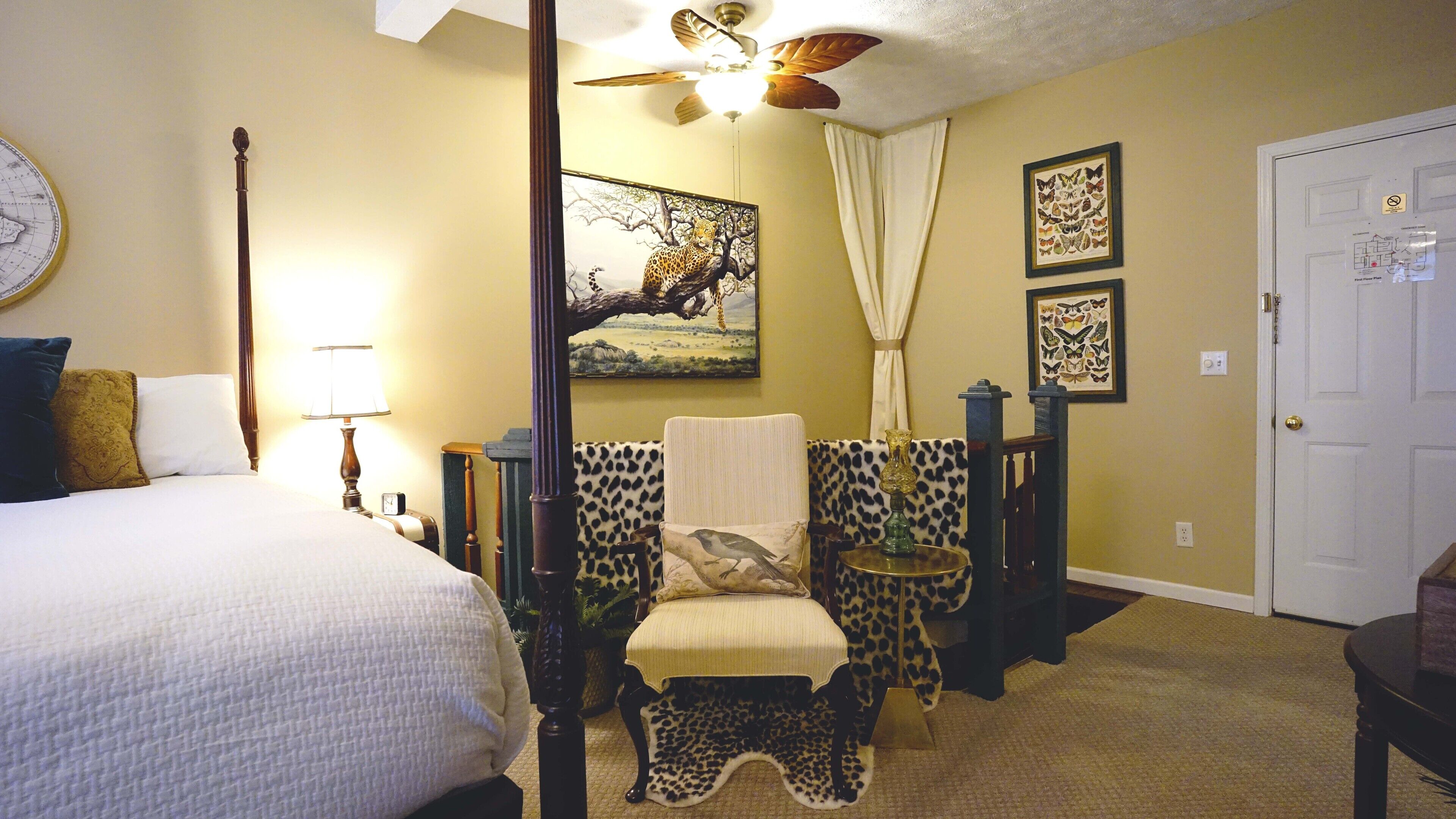 A bedroom with a bed, a nightstand, a chair, a ceiling fan, and a door.