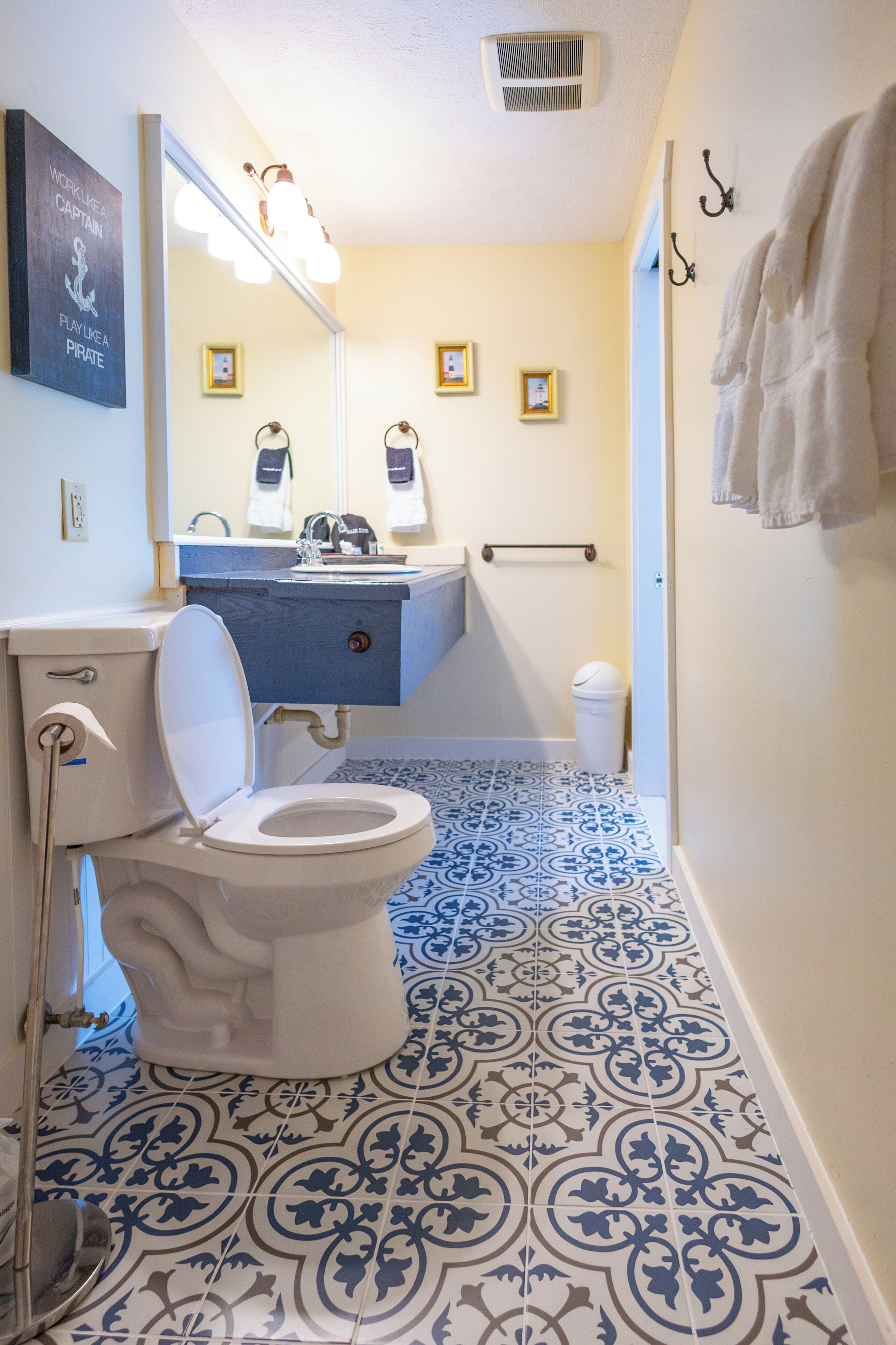 Un baño con inodoro, lavabo y espejo. El suelo tiene baldosas con un diseño azul y blanco.