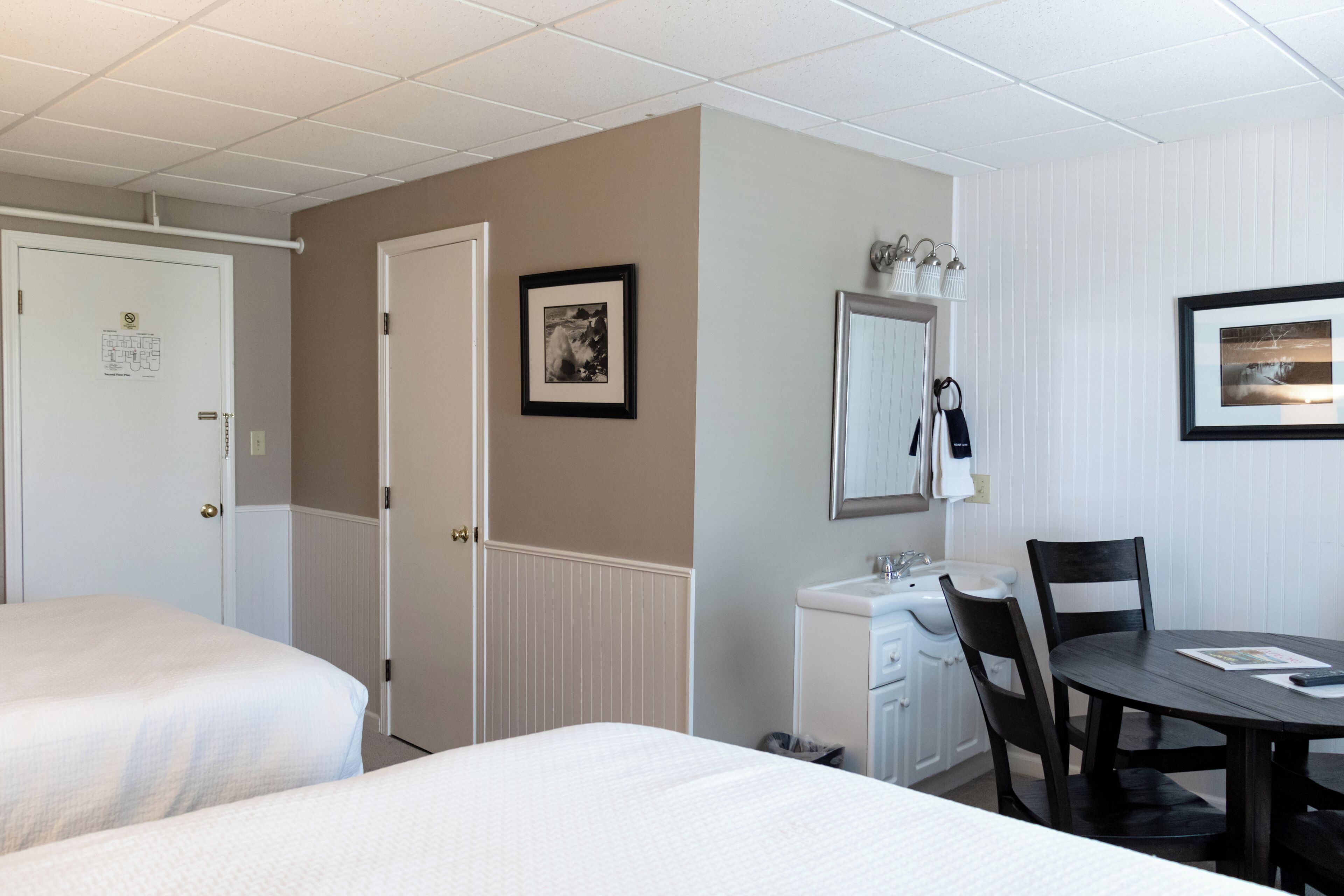 A hotel room with two beds, a small desk with a mirror, and a dining table with chairs.
