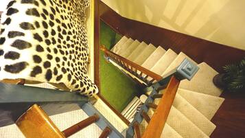 Una escalera con barandilla de madera, peldaños alfombrados y un rellano cubierto de alfombra verde.