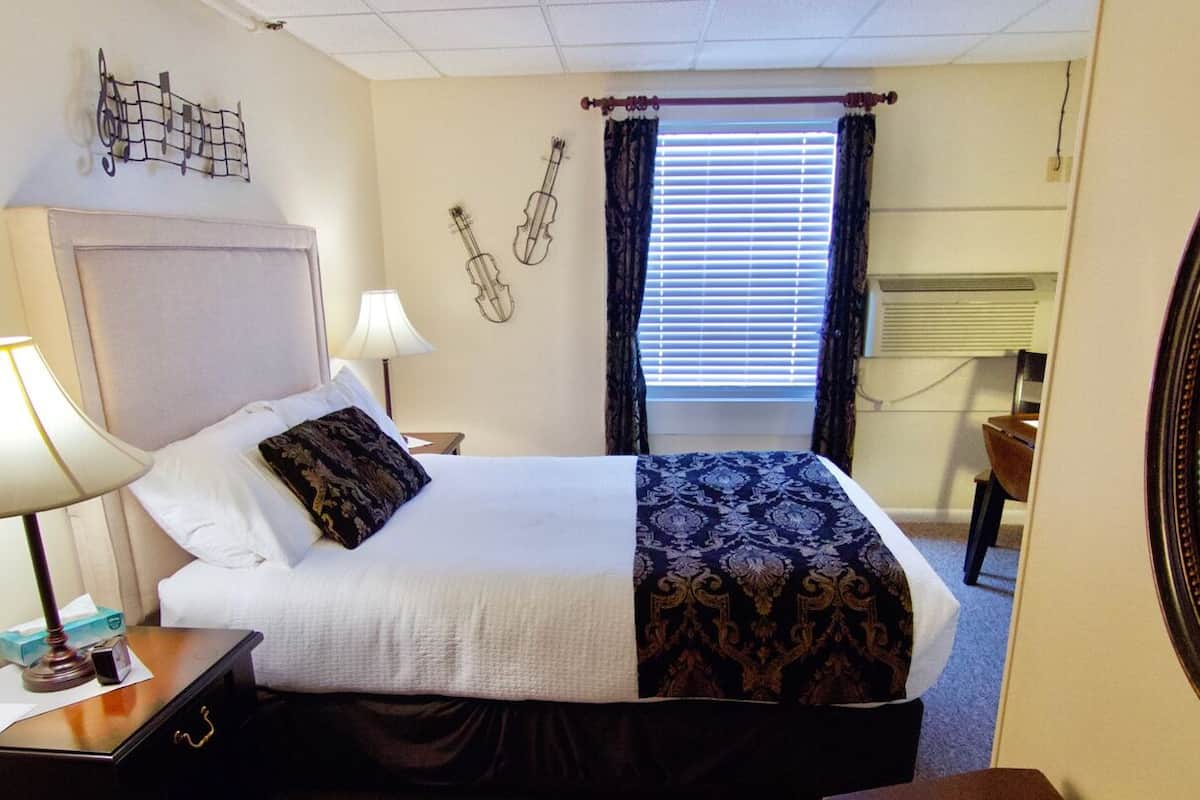 Hotelkamer met een bed, twee bedlampen, een spiegel, een raam met gordijnen en een gitaardecoratie aan de muur.