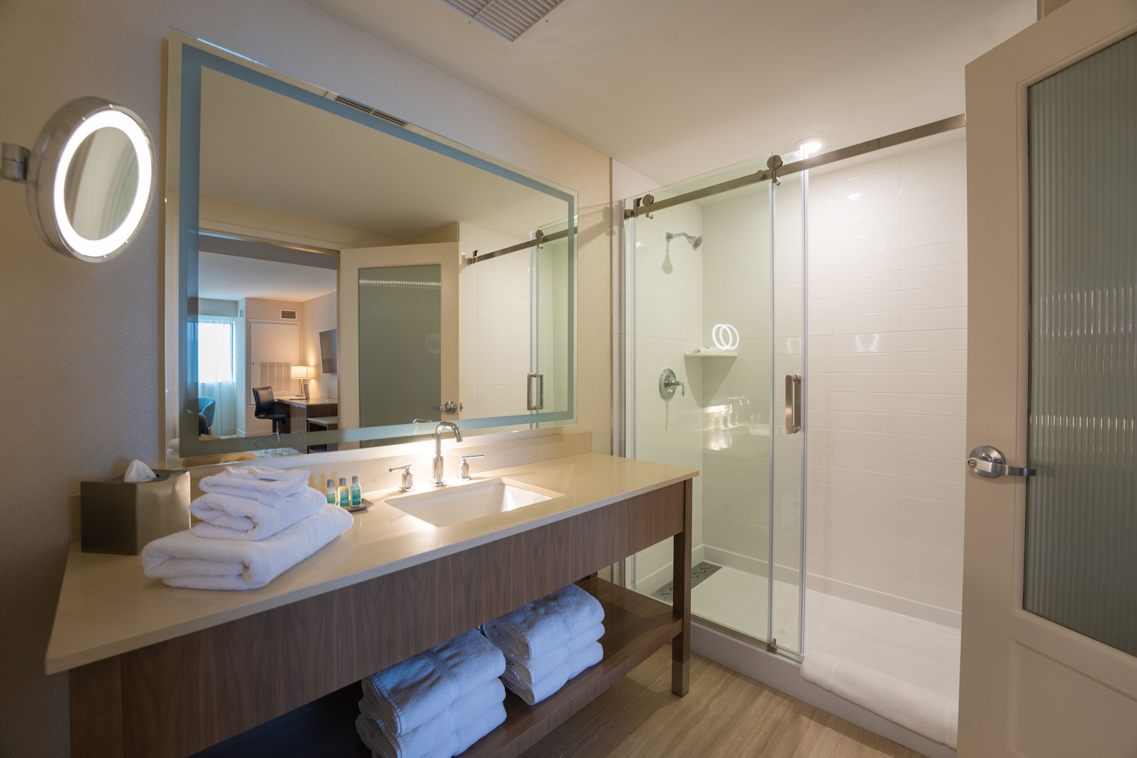 A modern bathroom with a large mirror, a sink, and a glass shower enclosure.