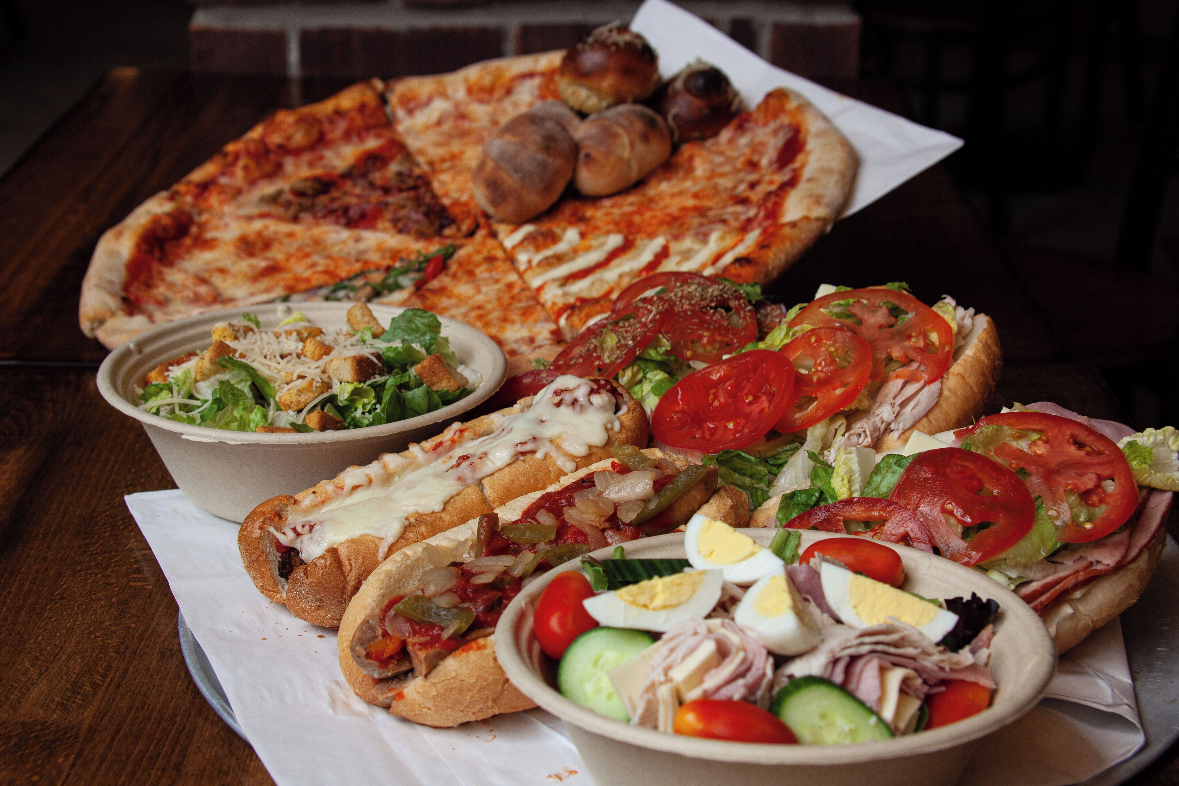 A variety of food items including a pizza, sandwiches, and salads on a table.