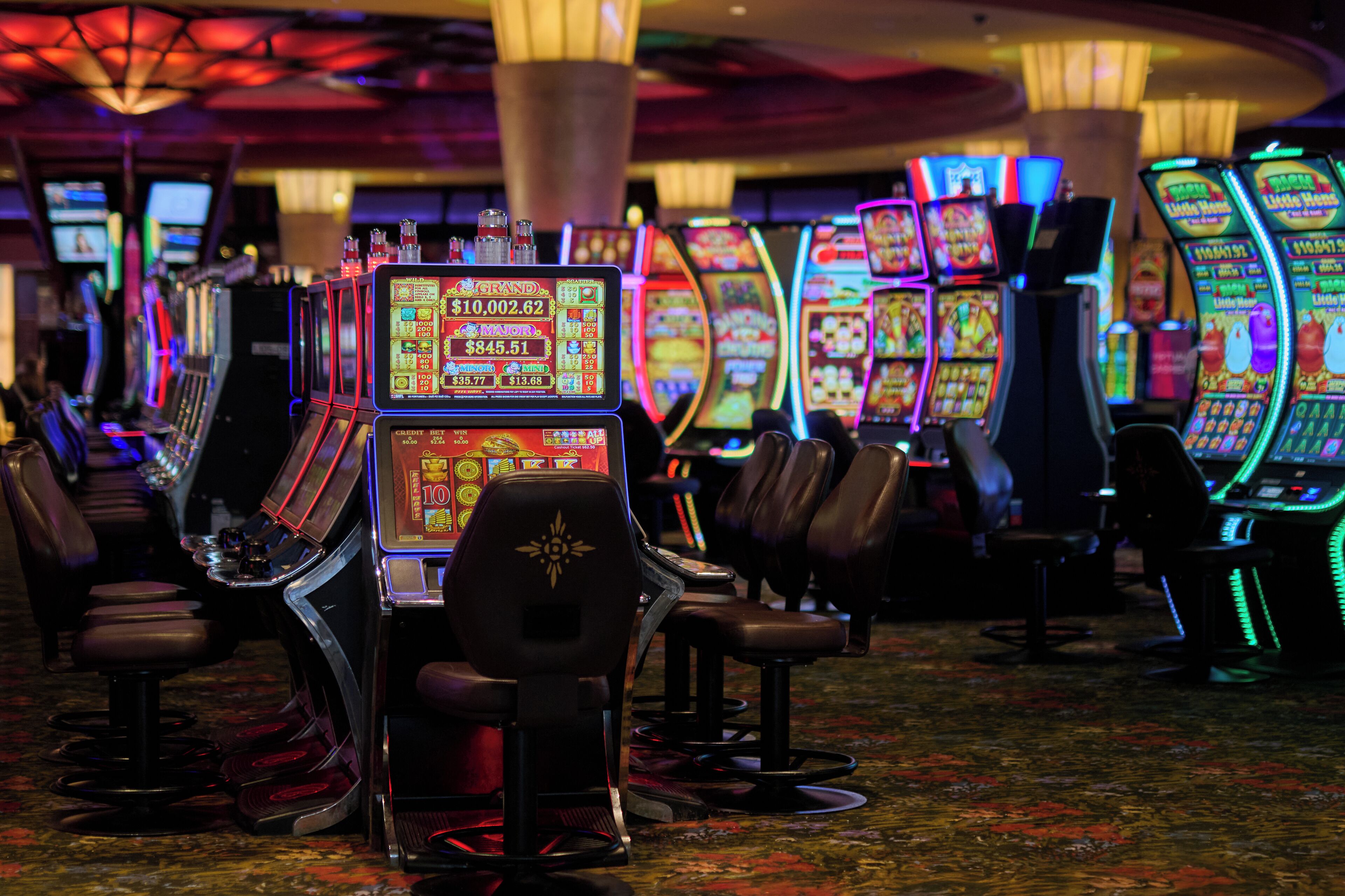 Une rangée de machines à sous dans un casino, avec des chaises devant.