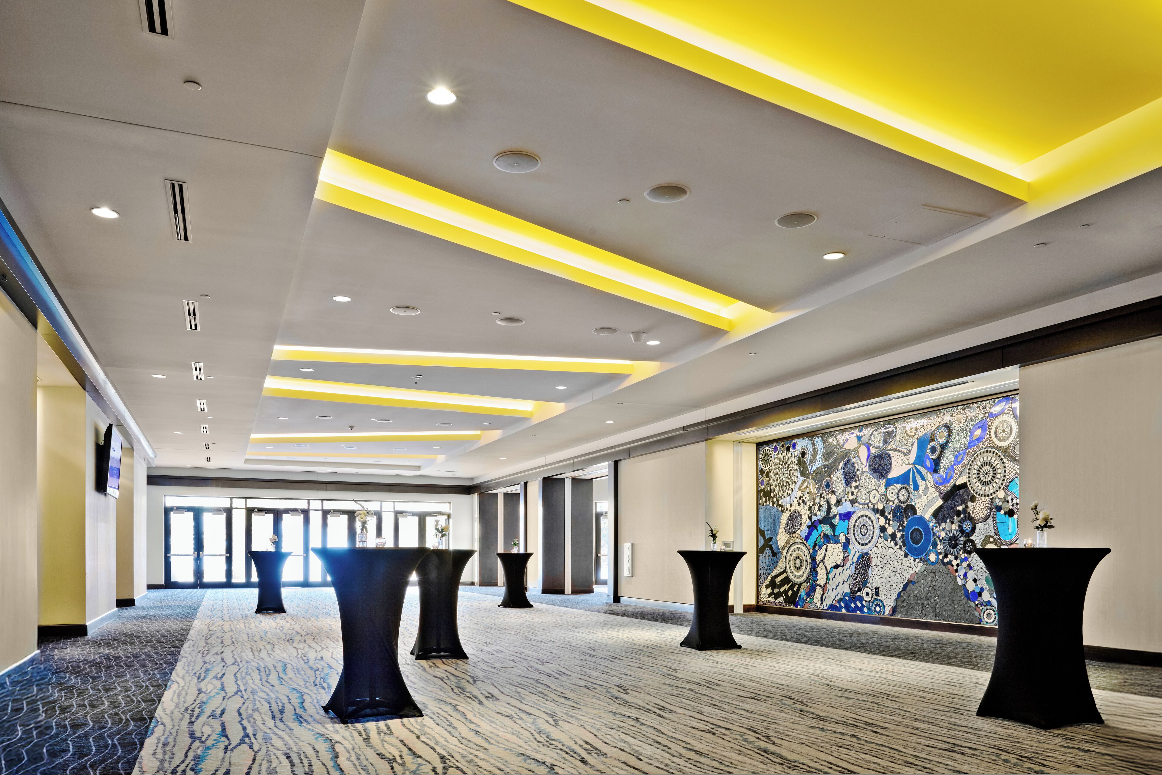 Un vestíbul d'hotel espaiós, amb un sòl de marbre, un disseny de sostre modern i il·luminació groga, i un mural decoratiu a la paret.