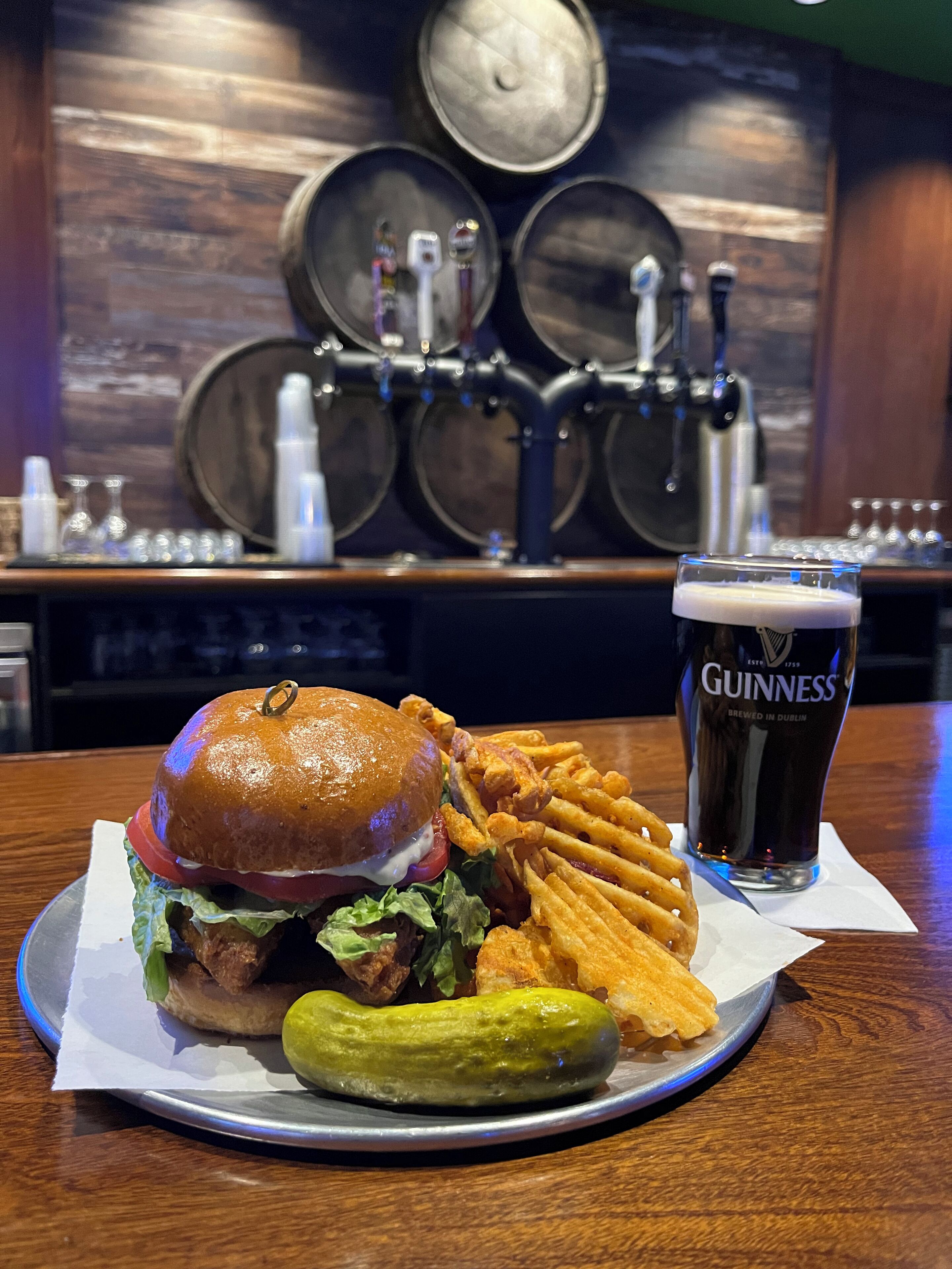 Un repas composé d’un hamburger, de frites, d’un cornichon et d’un verre de bière Guinness, le tout posé sur une table.