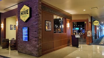 Un hall d’hôtel avec une enseigne indiquant « The Hive Taphouse », des panneaux de bois, un menu numérique et un bar visible à travers la vitre.