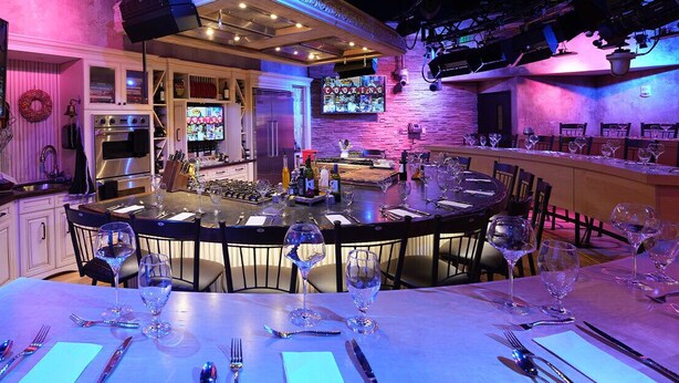 A bar area with a central island, bar stools, and a television displaying a cooking show.