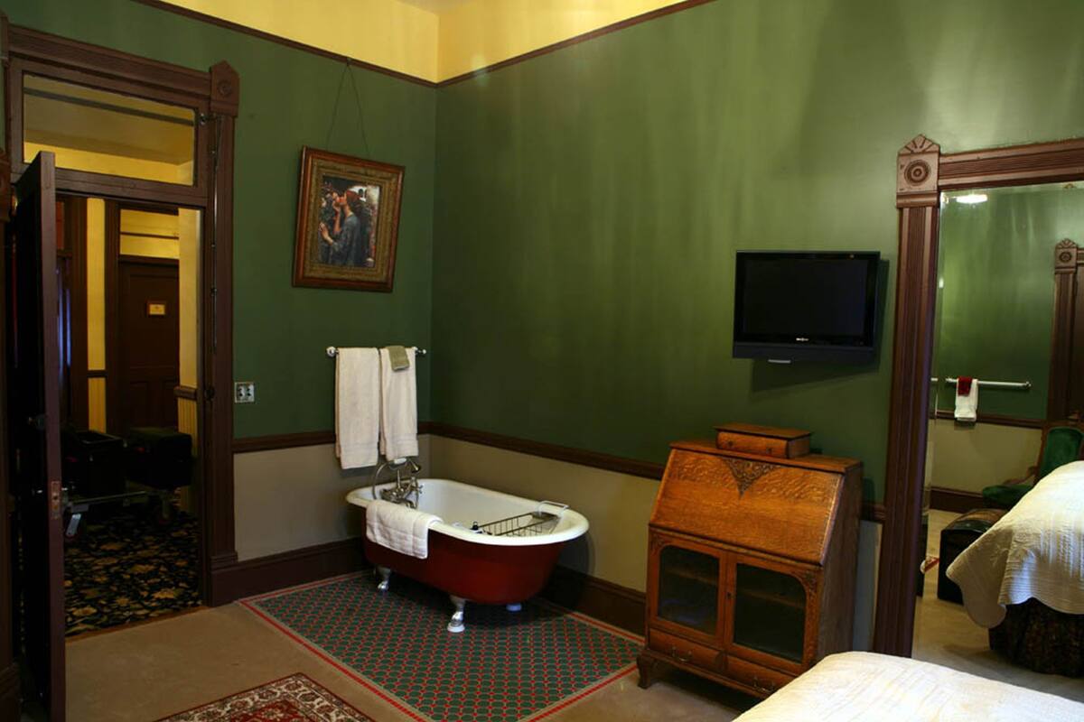 A bathroom with a bathtub, a wooden cabinet, a television mounted on the wall, and a mirror.