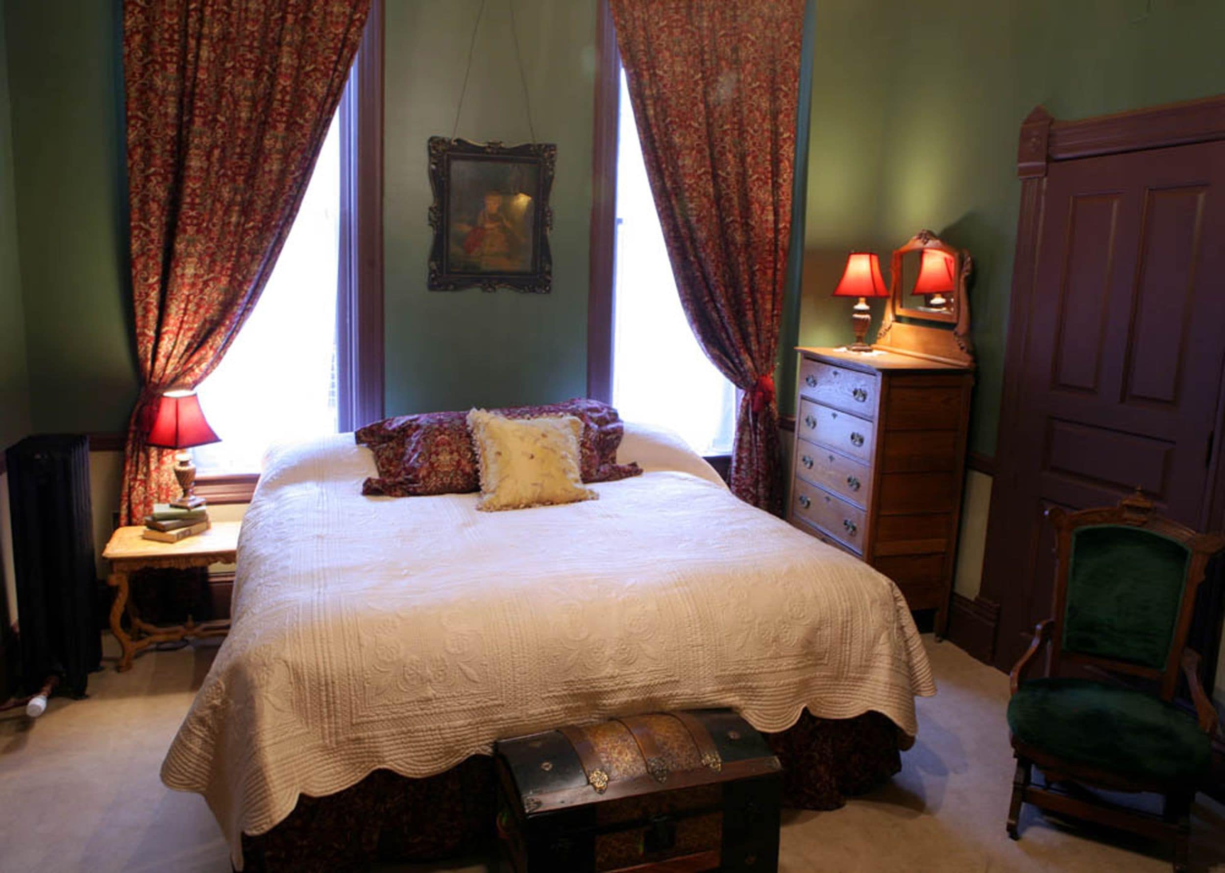 A bedroom with a large bed, a dresser, a chair, and a window with curtains.