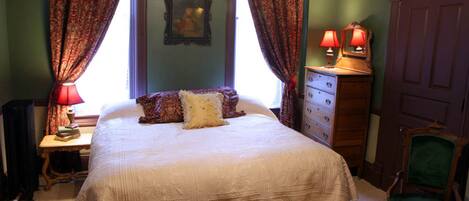 A bedroom with a large bed, a dresser, a chair, and a window with curtains.