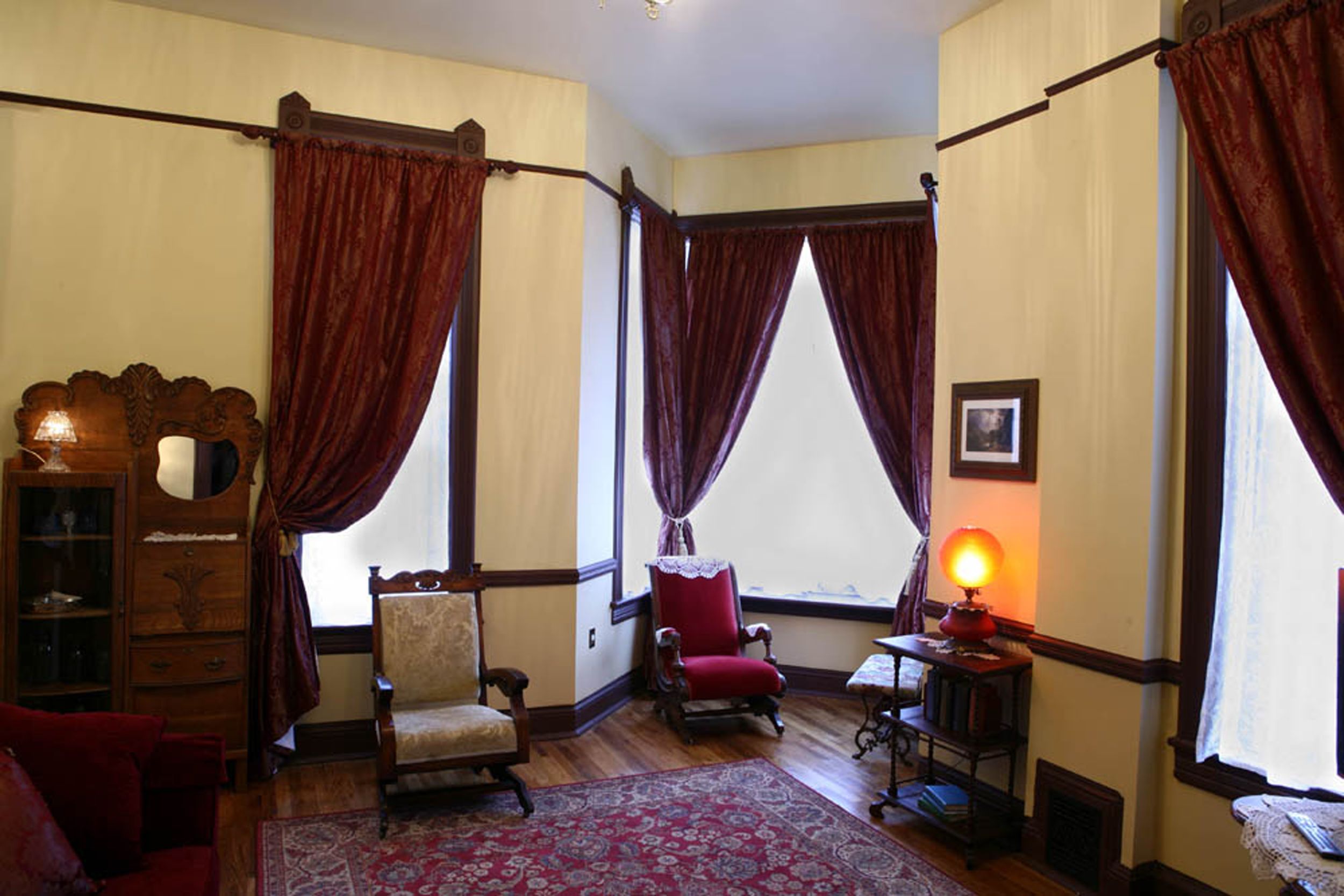 A room with two chairs, a small table with a lamp, and a wooden cabinet.