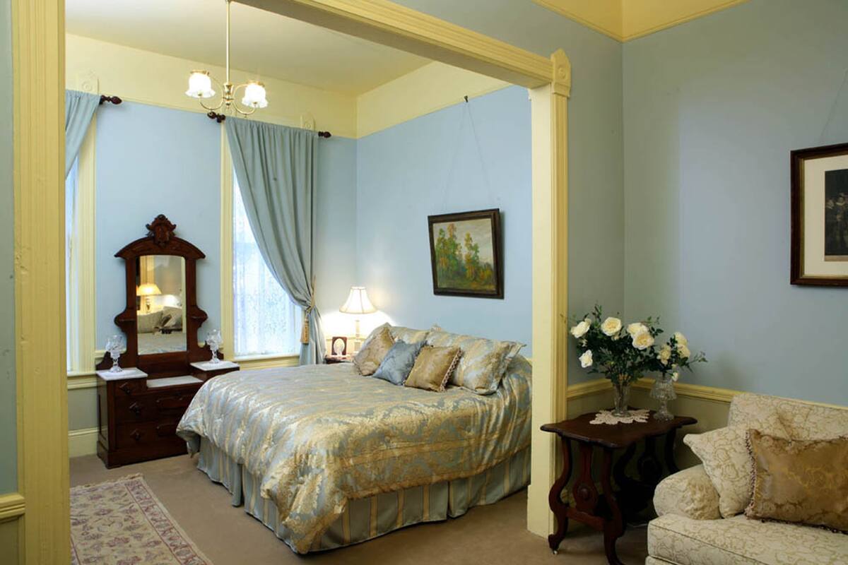A bedroom with a large bed, a dresser, a mirror, a nightstand, a lamp, and a vase with flowers.
