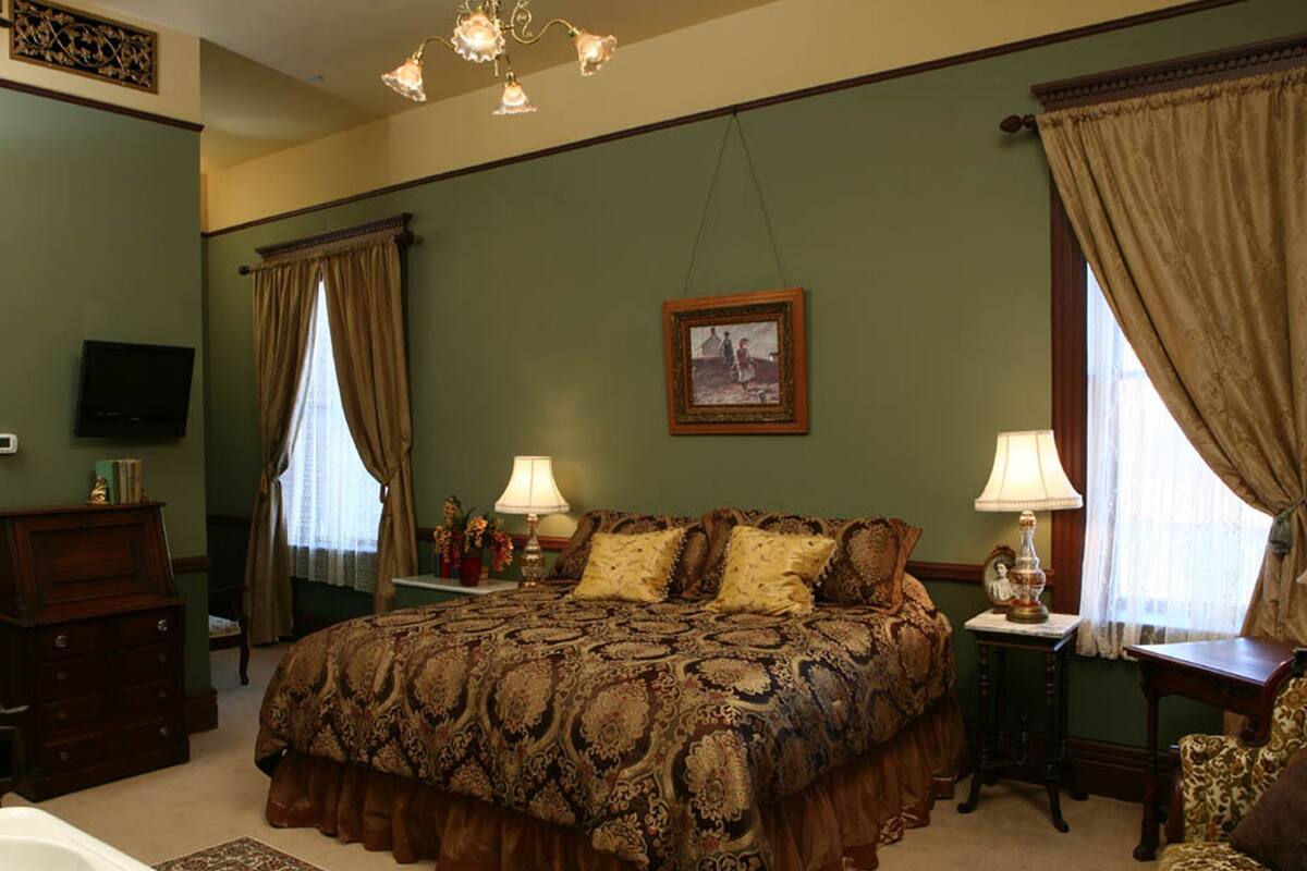 A bedroom with a large bed, two bedside tables, a dresser, a television, and a chandelier.