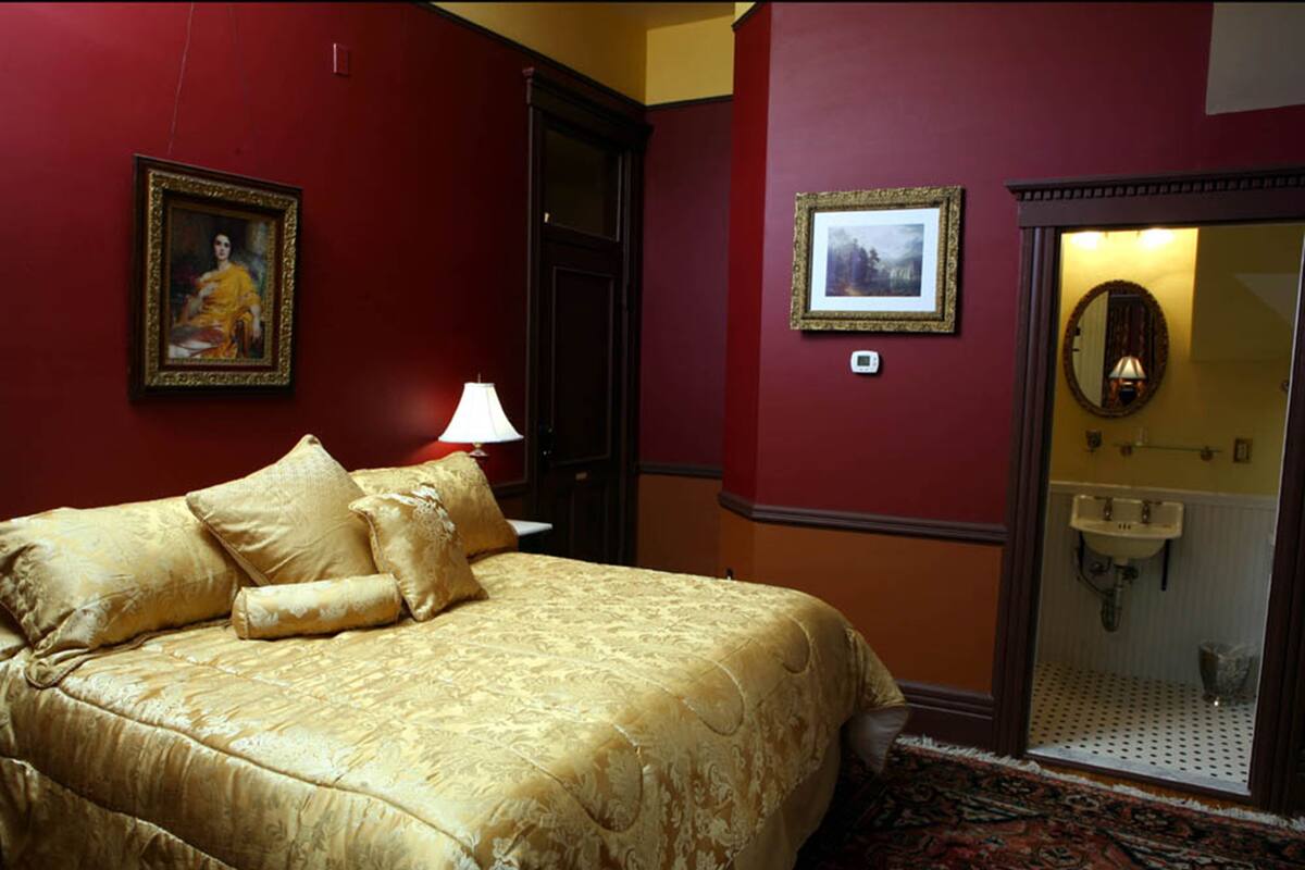 A hotel room with a large bed, a bathroom with a mirror and sink, and two framed pictures on the walls.