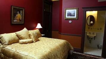 A hotel room with a large bed, a bathroom with a mirror and sink, and two framed pictures on the walls.