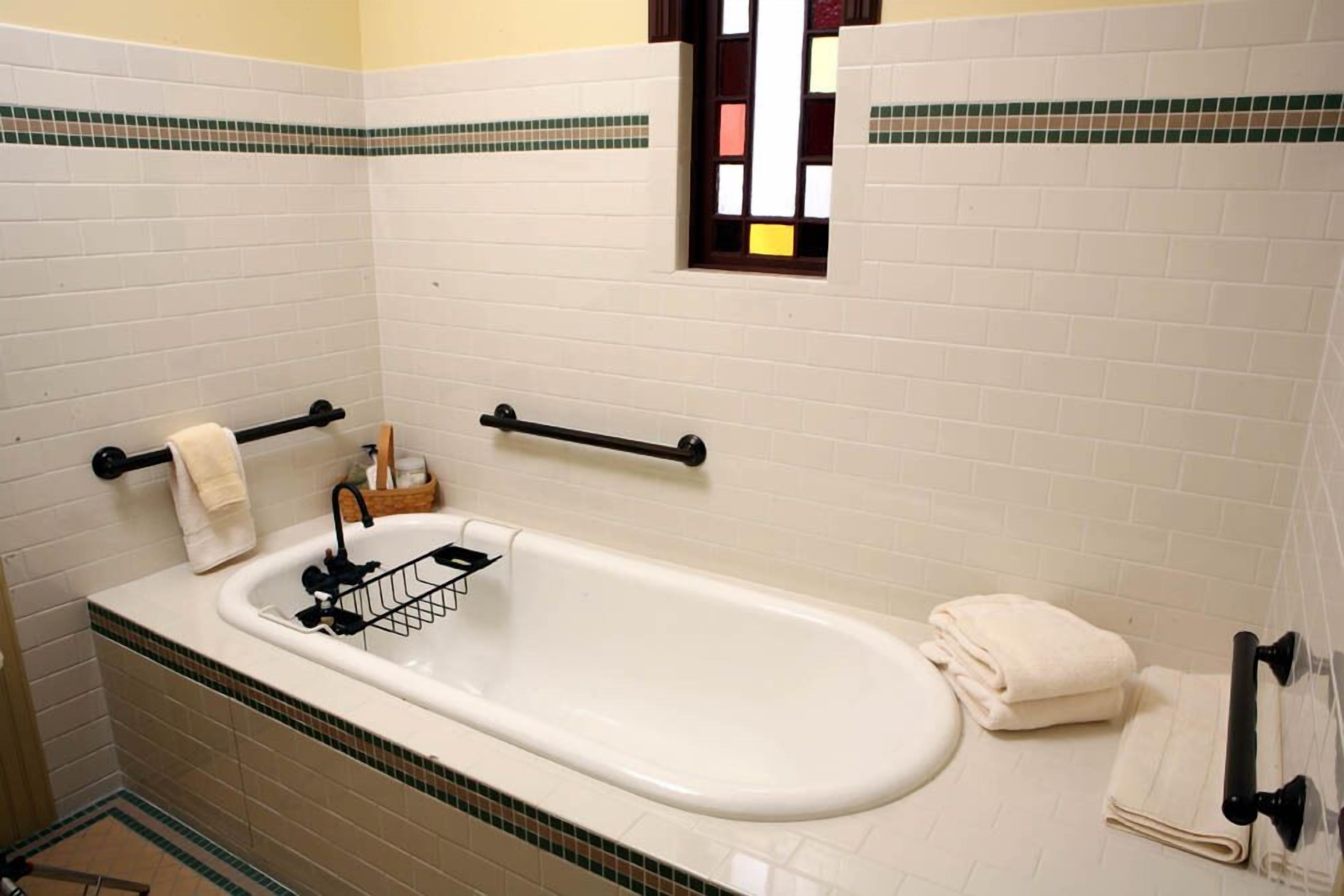 A bathroom with a white bathtub, a towel rack, a window, and a tiled floor.