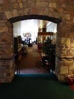 A stone archway leading to a lobby with a patterned carpet, a Christmas tree, and a seating area with a table and chairs.