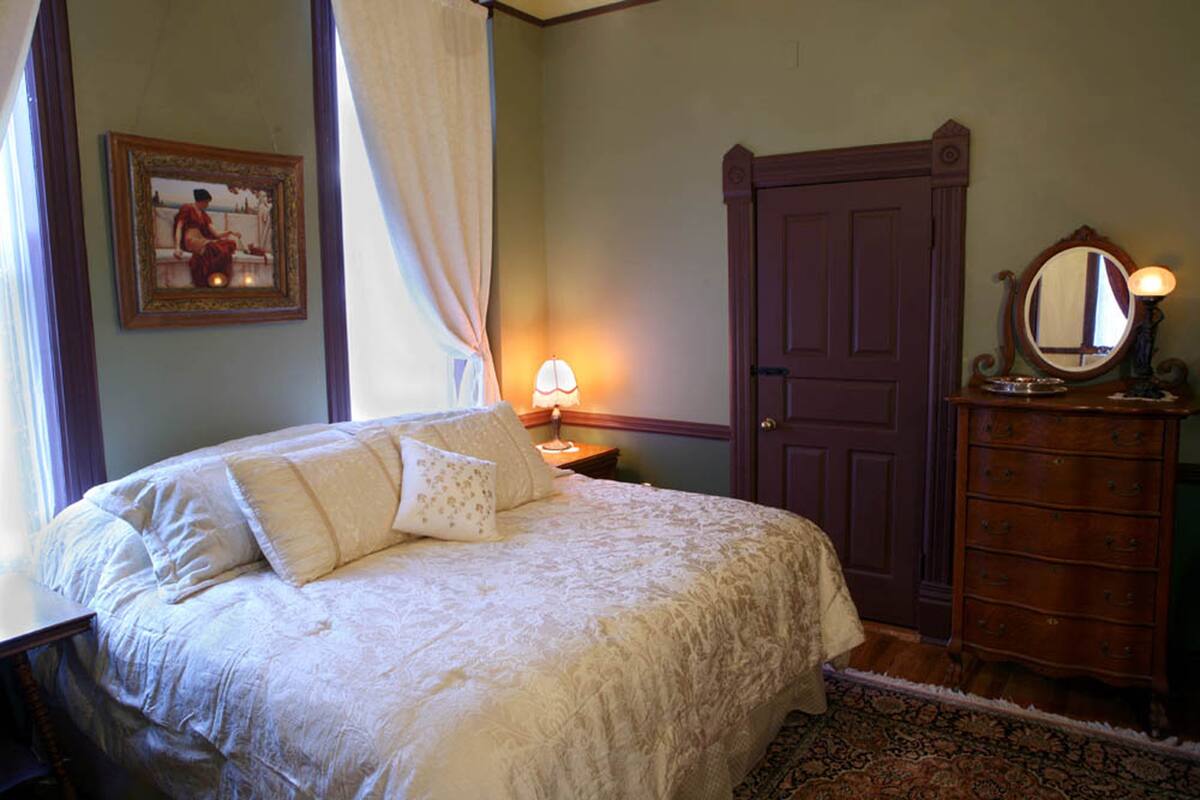 A bedroom with a large bed, a dresser, a mirror, and a framed picture on the wall.
