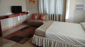 A hotel room with a bed, a sofa, a television, and a window with curtains. - GE Home Residential Inn (Cebu City)