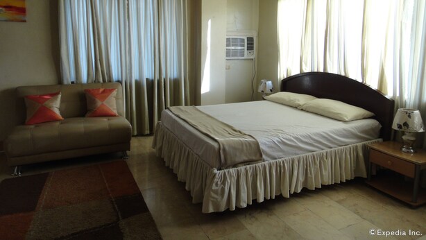 A bedroom with a bed, a sofa, a nightstand, and curtains. - GE Home Residential Inn (Cebu City)