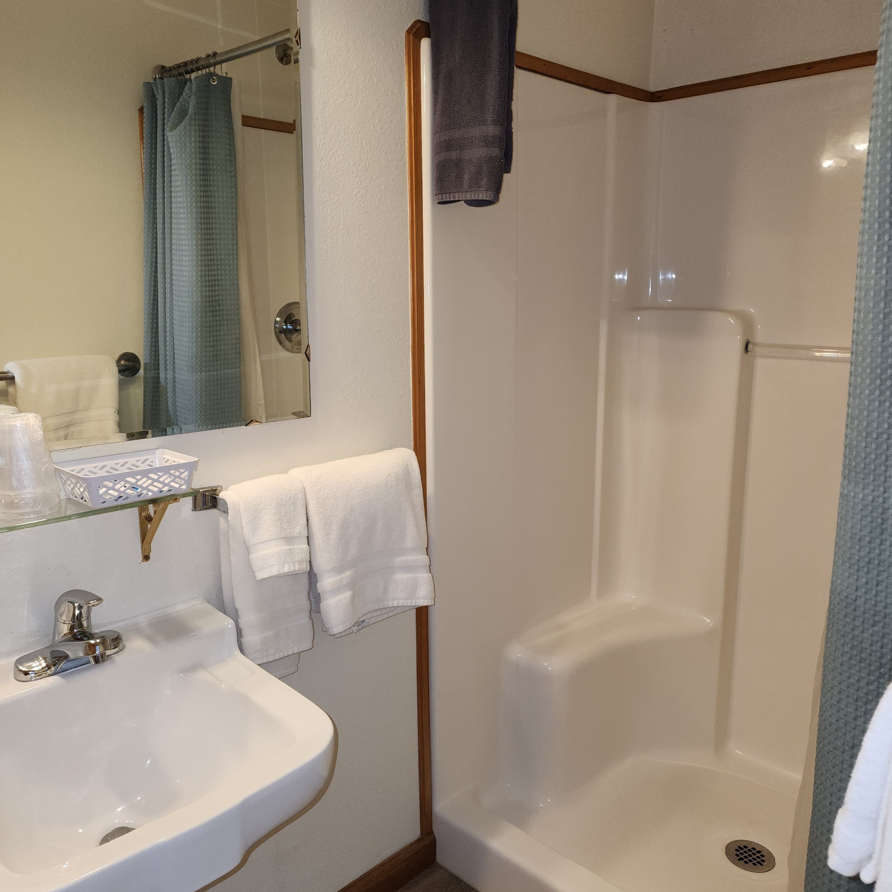 Un baño con lavamanos blanco, un espejo, ducha con puerta de cristal y toallero.