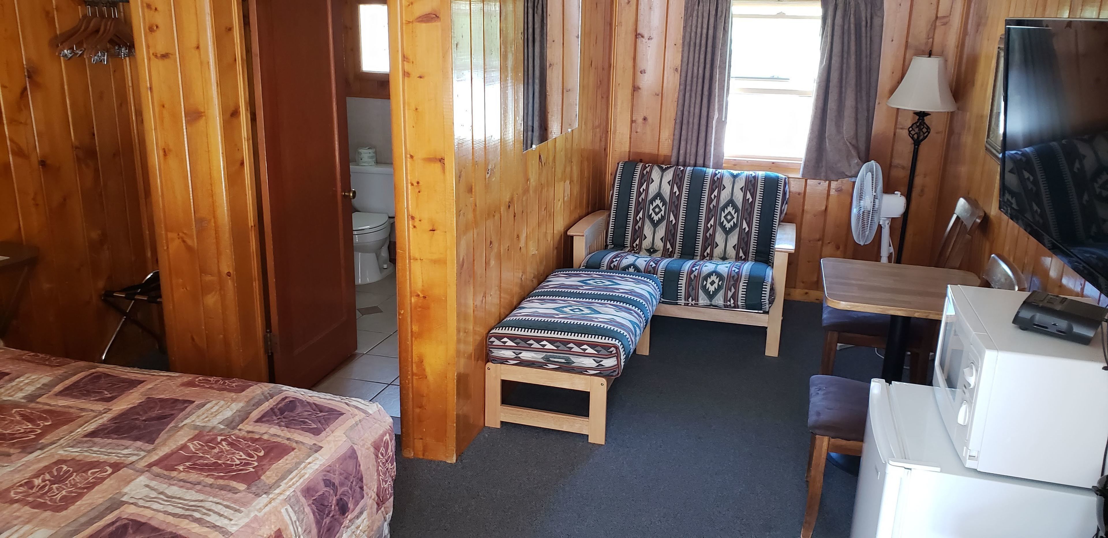 Una habitación con paneles de madera, una cama, un sofá, un escritorio, un televisor y un ventilador.