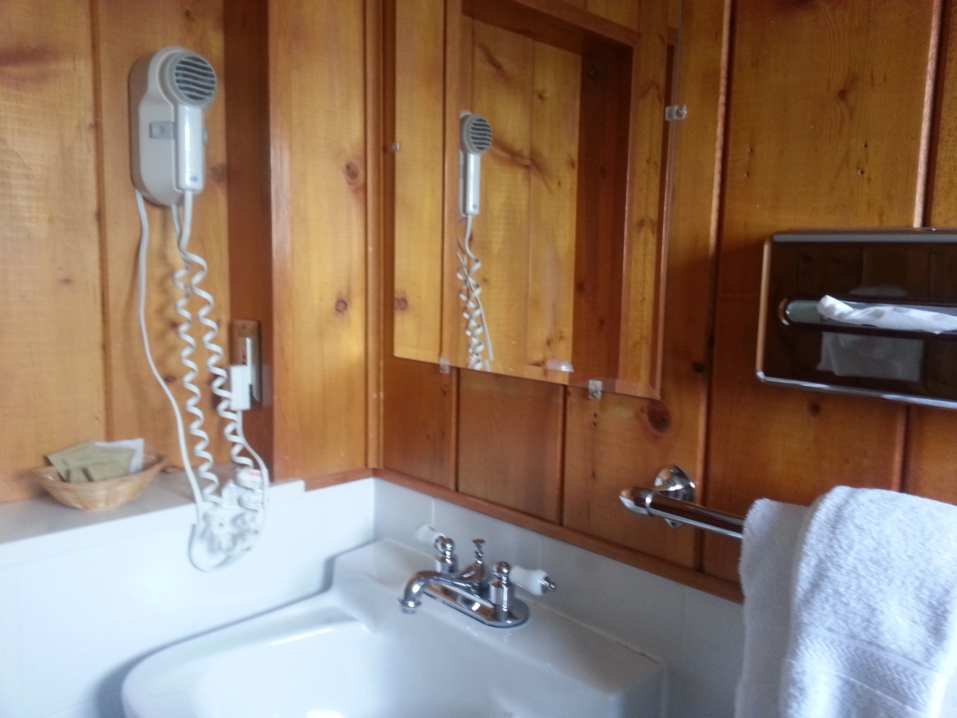 Un baño de madera con un lavabo blanco, un secador de pelo y un espejo.